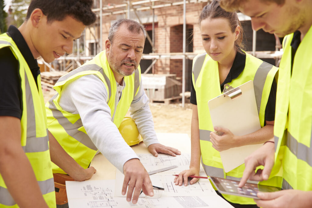 Mehrere bauarbeiter und die fachkraft für Arbeitssicherheit sprechen auf der Baustelle über den Arbeitsschutz