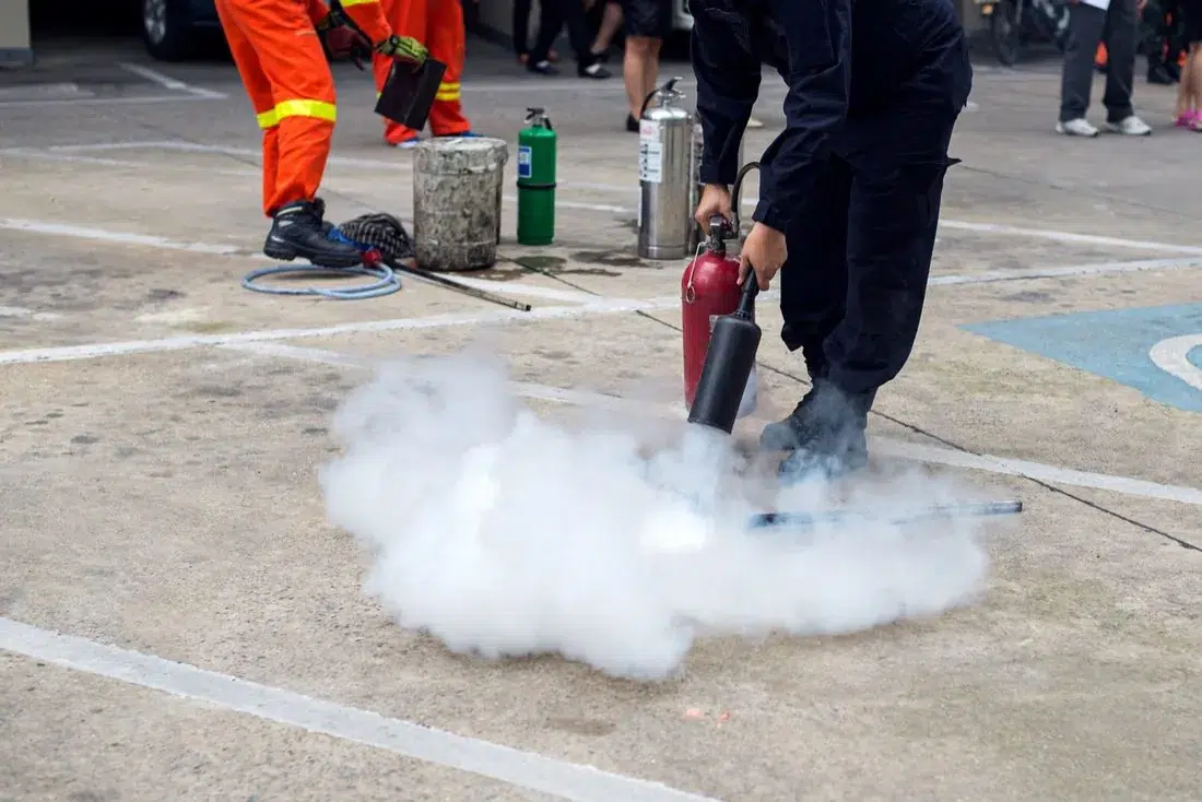Teilnehmer einer Brandschutzhelfer-Ausbildung üben mit einem Feuerlöscher im Freien