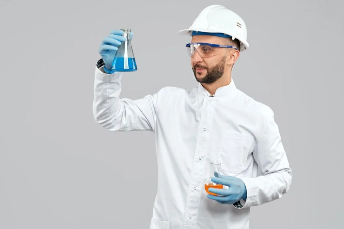 Mitarbeiter mit Schutzbrille und Handschuhen prüft eine Flüssigkeit im Kolben