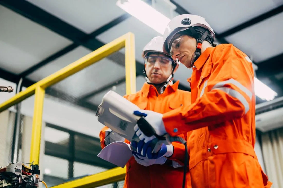 Zwei Mitarbeiter in Schutzkleidung mit Helm in einer Industriehalle