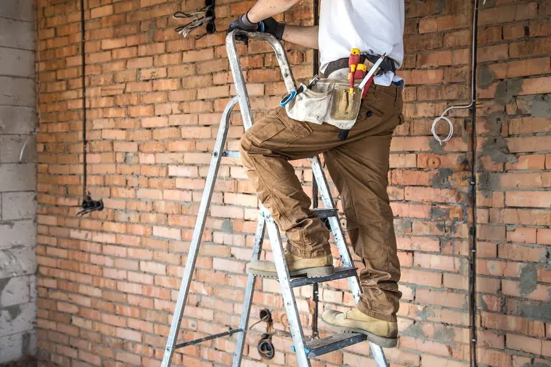 Handwerker mit Werkzeuggürtel auf einer Stehleiter