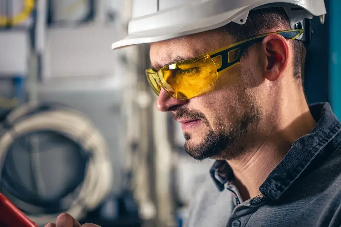 Elektrofachkraft mit Helm und Schutzbrille an einer Anlage